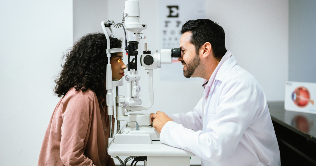 A patient and an eye doctor sit at a slit lamp in an exam room.